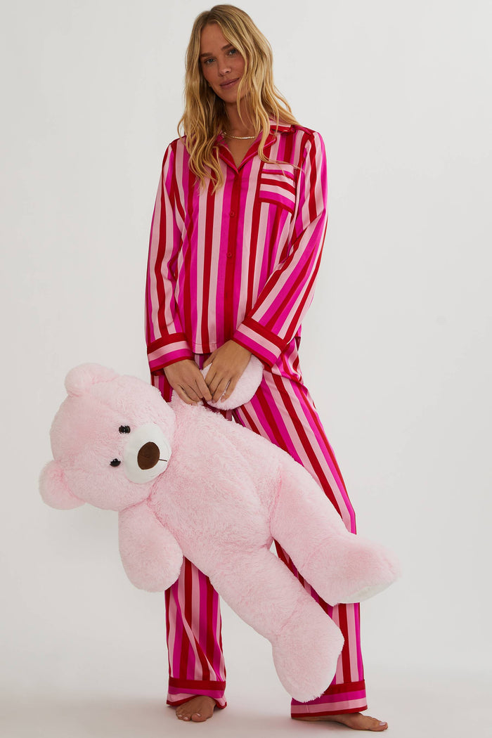 Woman in pink and white striped pajamas holding a large pink teddy bear against a white background
