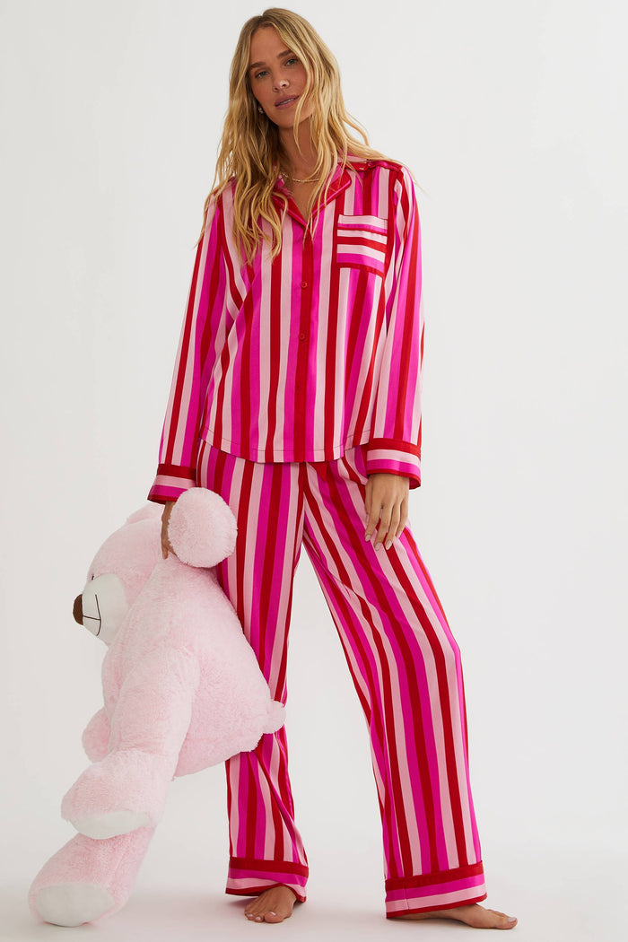 Woman wearing pink and white striped pajamas holding a pink teddy bear on a white background