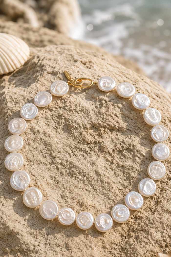A beaded necklace made of irregular, pearly white shell-like beads with a small gold clasp, shown on a plain white background.