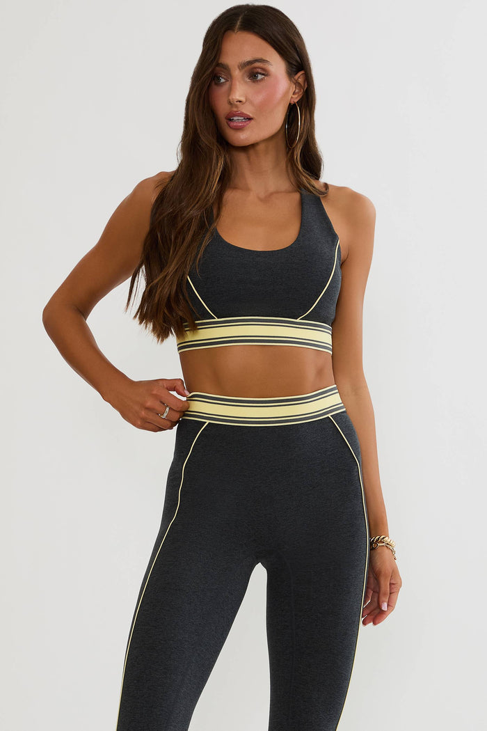 Woman wearing a black and yellow sports bra and leggings on a white background