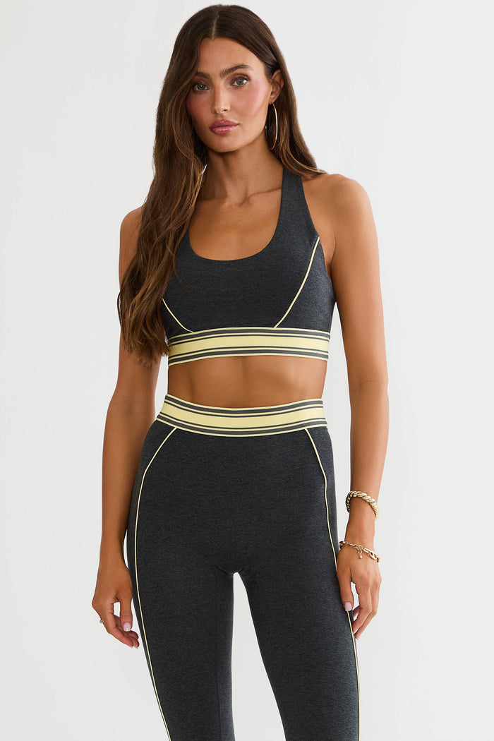 A woman modeling a dark gray athletic set consisting of a sports bra and high-waisted leggings with beige and dark gray striped accents.