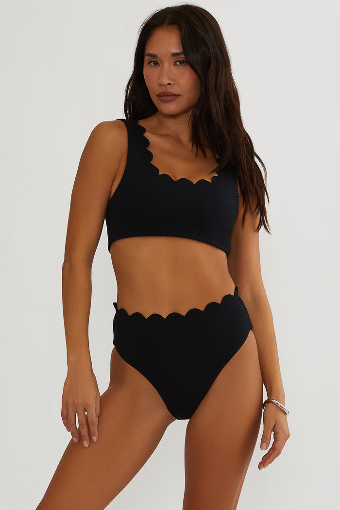 Woman wearing a black scalloped bikini set on a white background