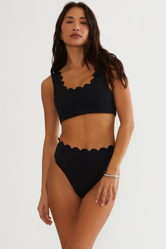 Woman wearing a black scalloped bikini set on a white background