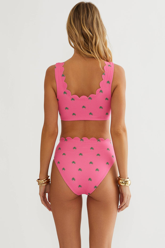 A woman shown from the back wearing a bright pink two-piece bikini with a scalloped neckline and a small gray leaf pattern, against a plain light gray studio background.