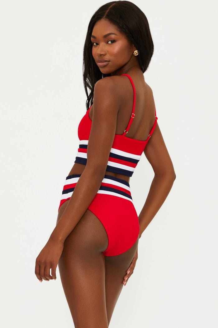 A woman sitting poolside wearing a red, white, and blue striped swimsuit top with adjustable straps.