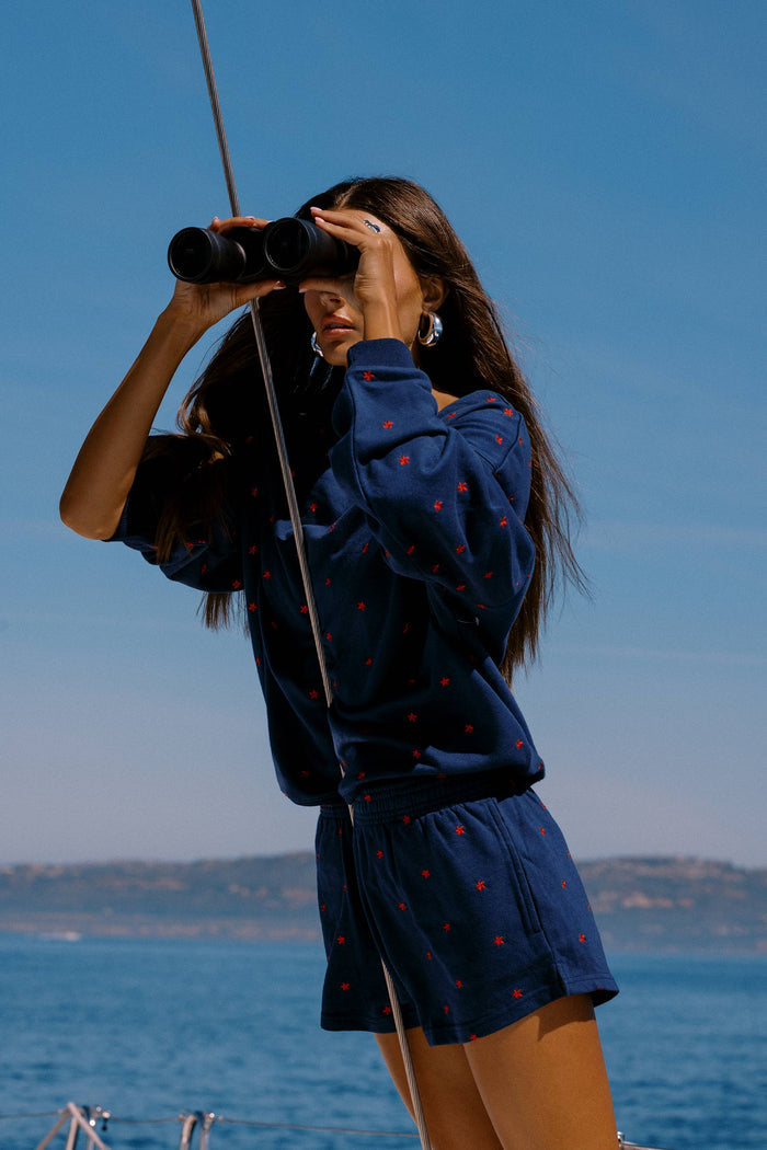Woman in a blue outfit with red patterns using binoculars by the ocean.