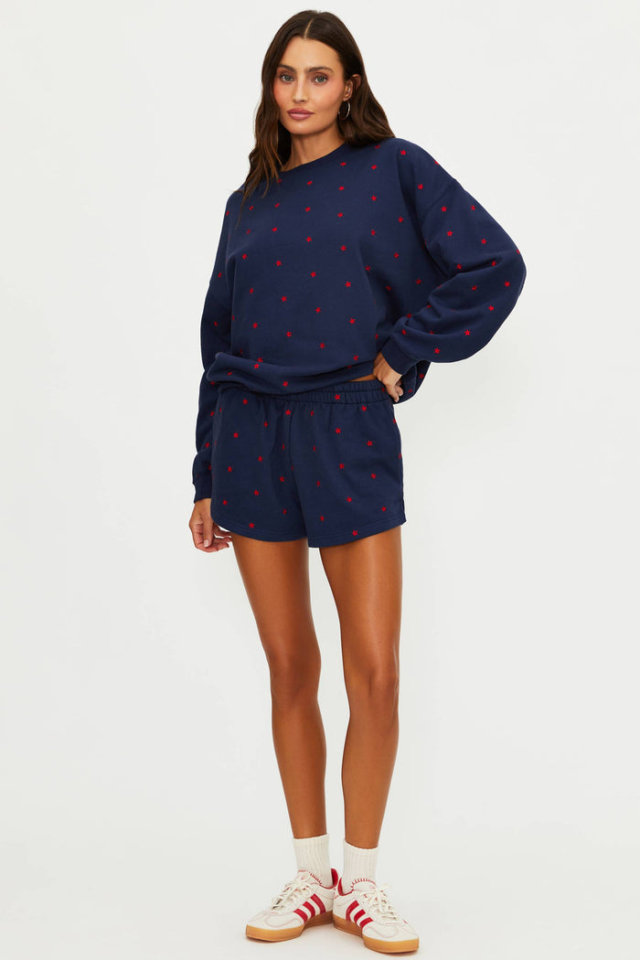 Woman wearing a navy sweatshirt and shorts set with red patterns on a white background