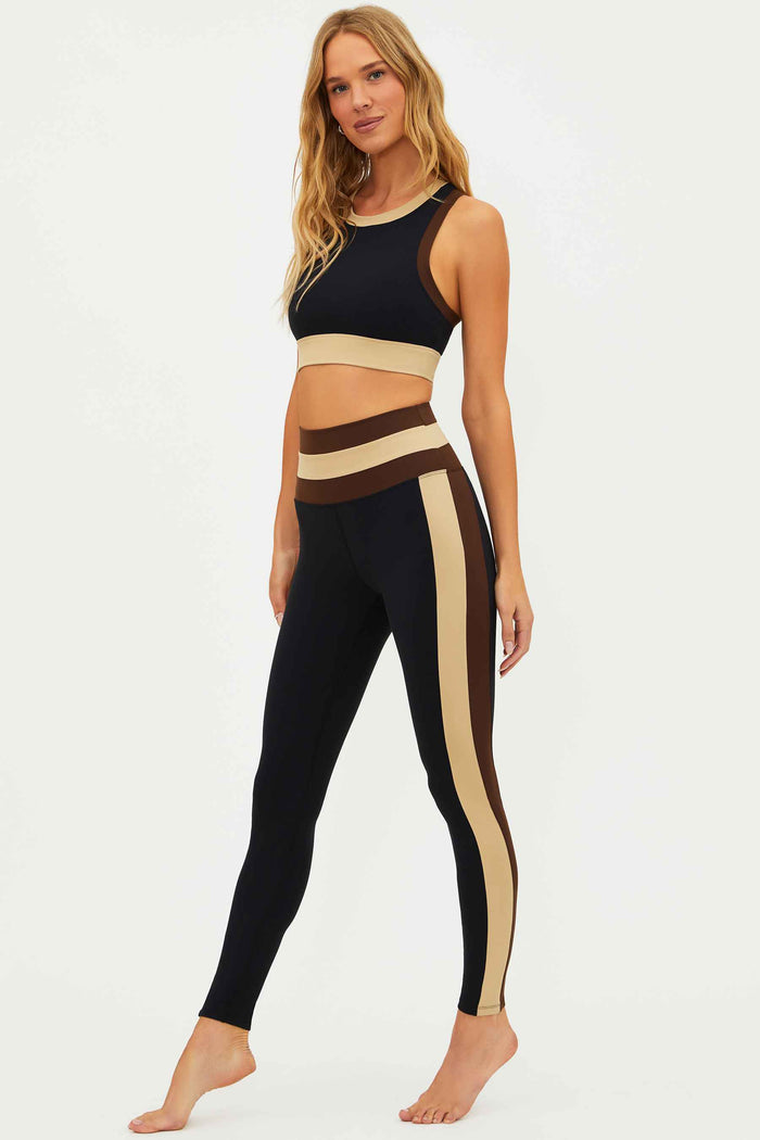 Woman wearing a black and beige sports bra and leggings set on a white background