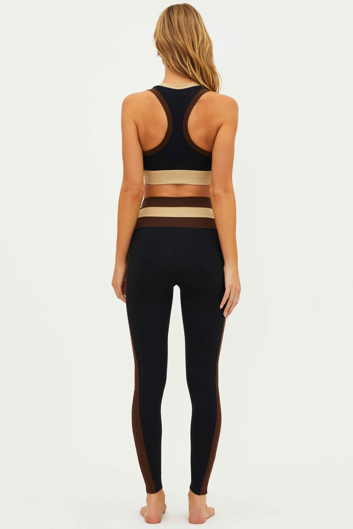 Person wearing a black sports bra and leggings with beige accents on a white background