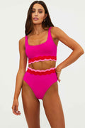 Woman wearing a bright pink swimsuit with scalloped details on a white background