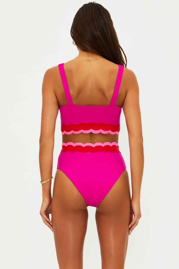 Woman wearing a bright pink bikini with scalloped edges on a white background