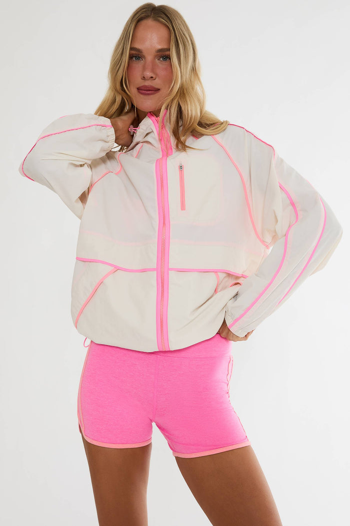 Woman wearing a white jacket with pink accents and pink shorts on a white background