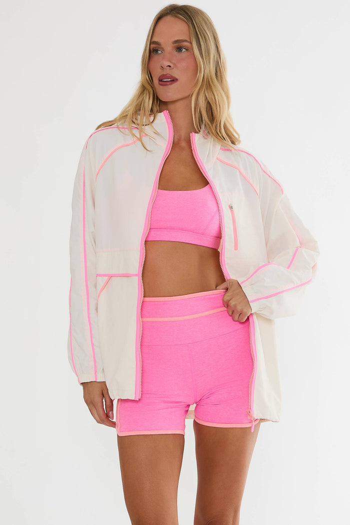 Woman wearing a pink sports outfit with a sheer white jacket on a white background