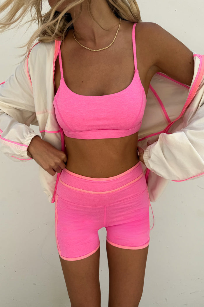 Person wearing a pink sports bra and shorts set with a light jacket.