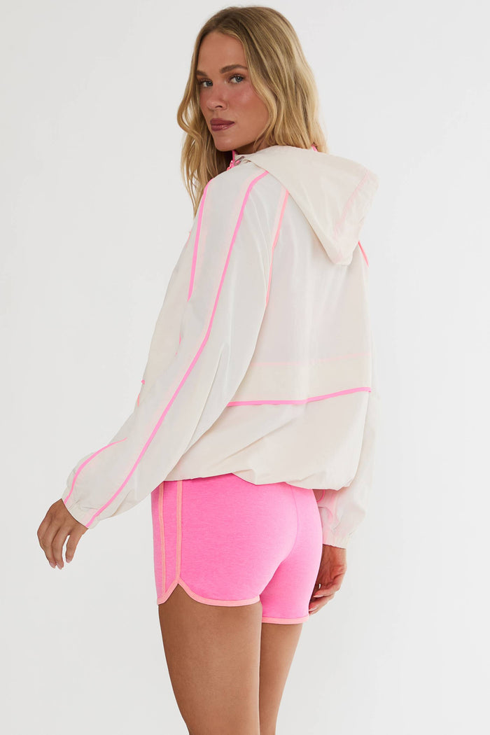 Woman wearing a white jacket with pink accents and pink shorts on a white background