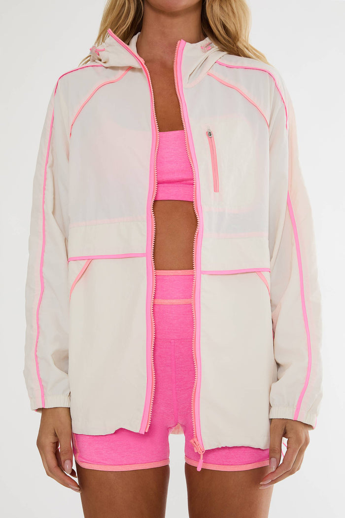 Person wearing a beige jacket with pink accents and matching pink shorts on a white background