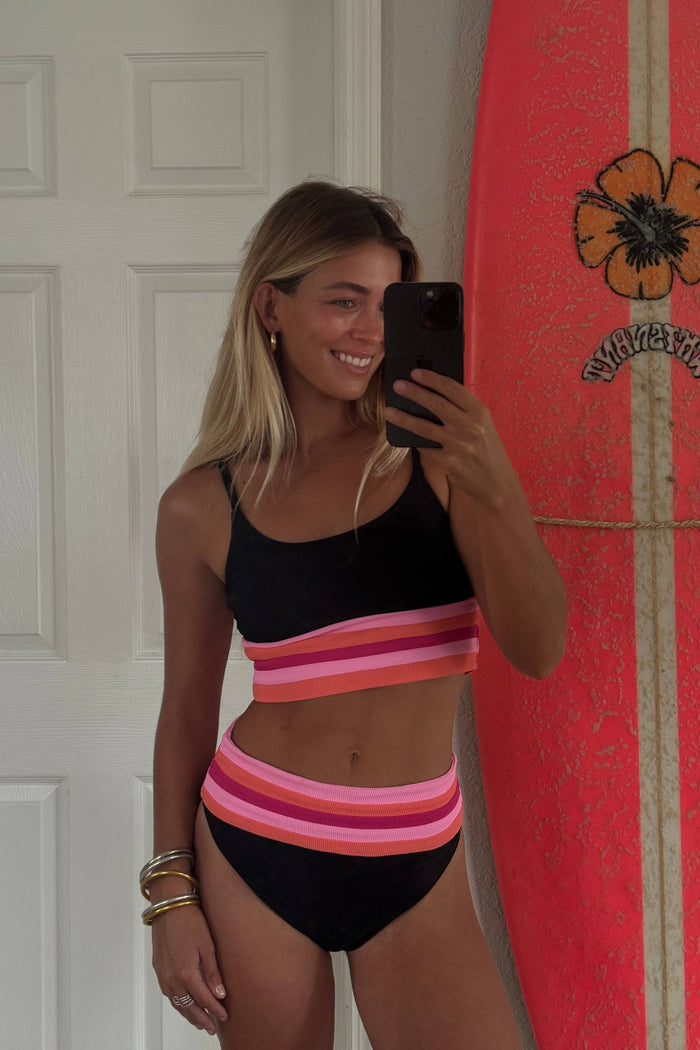Woman taking a mirror selfie wearing a colorful bikini in front of a red surfboard with a floral design.