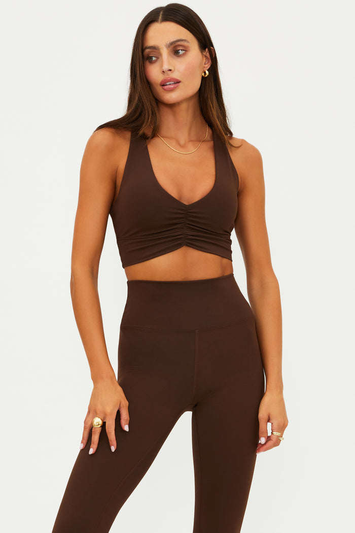 Woman wearing a brown sleeveless top and leggings on a white background