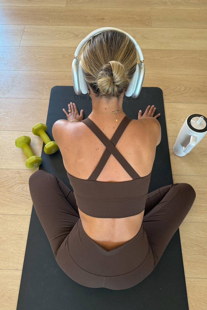 Person sitting on a yoga mat with headphones on, surrounded by dumbbells and a water bottle.