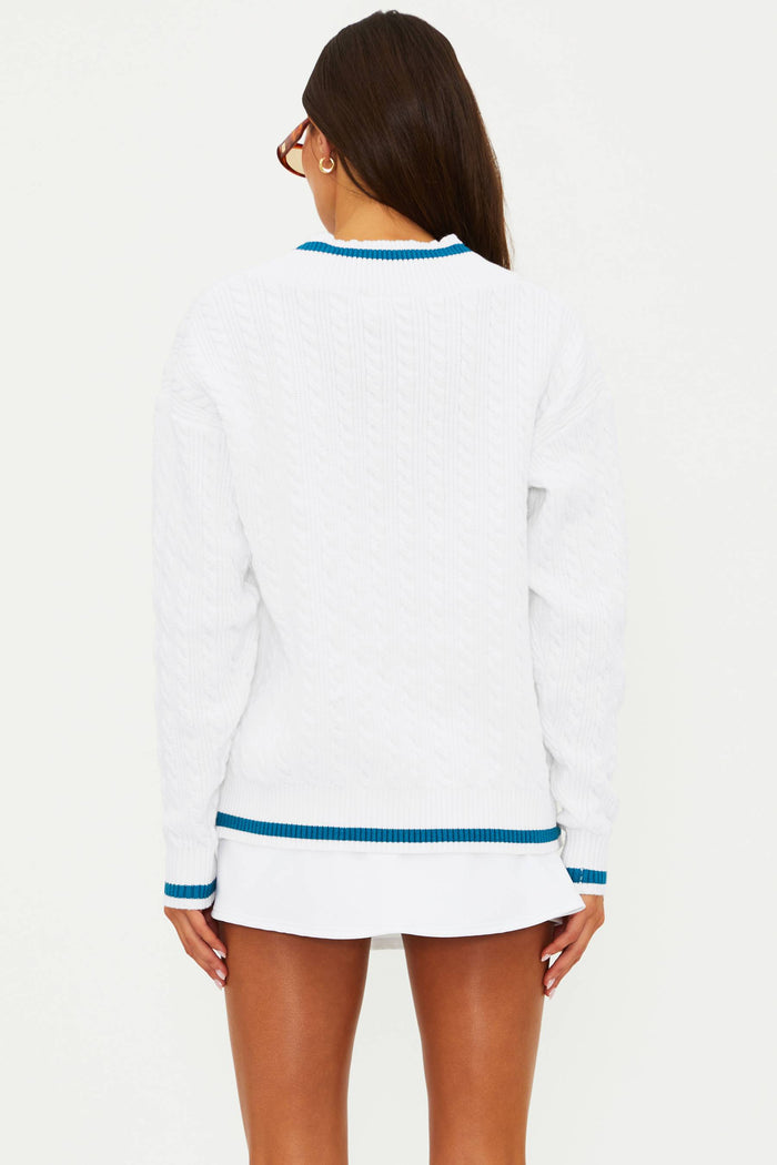 Woman wearing a white sweater with blue trim on a plain background
