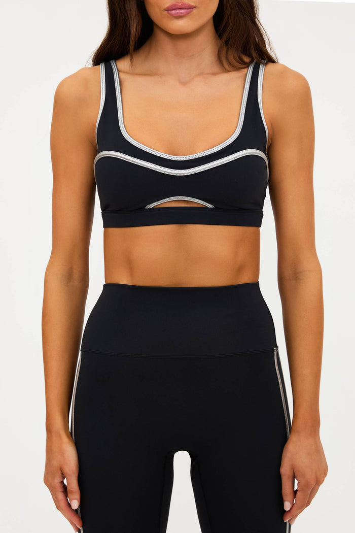 Person wearing a black sports bra and leggings with white accents on a white background