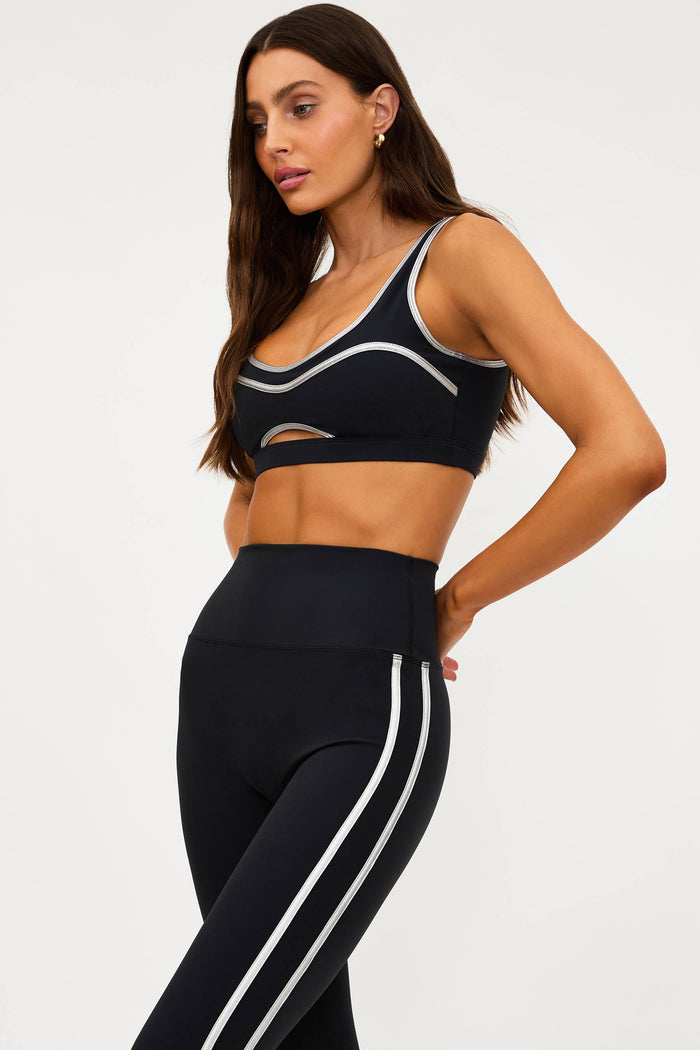 Woman wearing a black sports bra and leggings with white stripes on a light gray background
