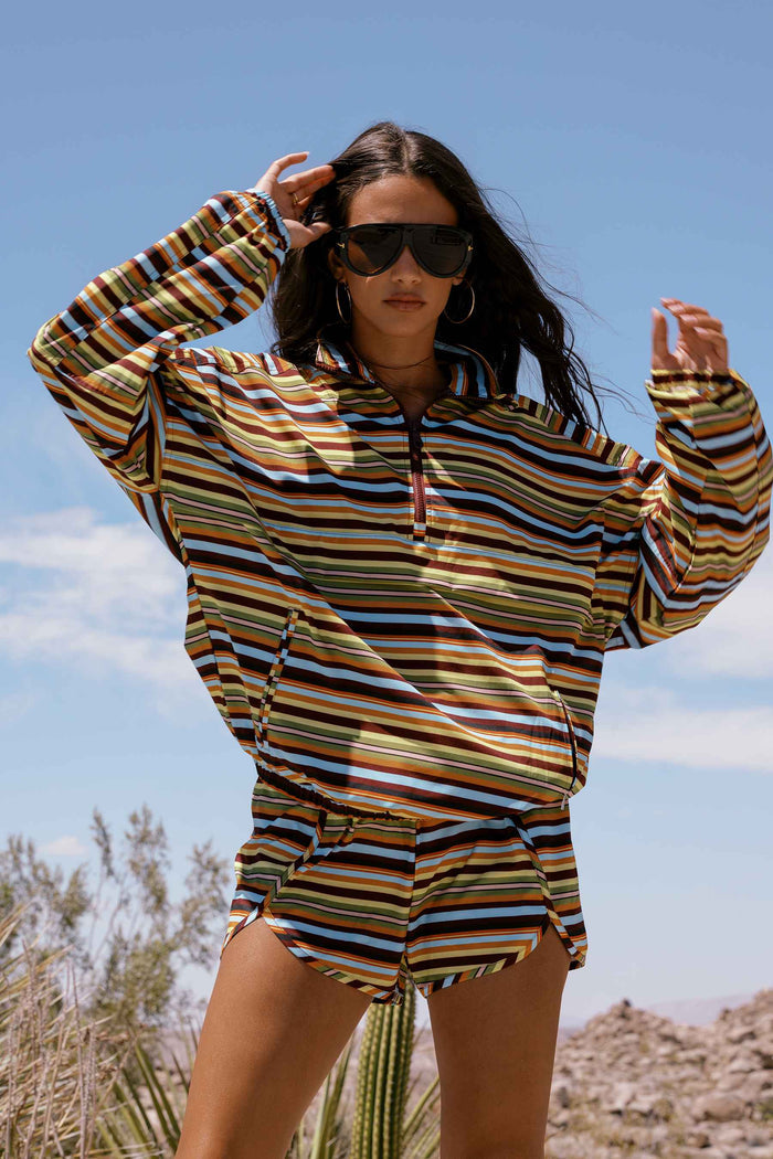 A woman wearing a matching long-sleeve striped quarter-zip pullover and shorts set in an outdoor desert landscape under a blue sky.