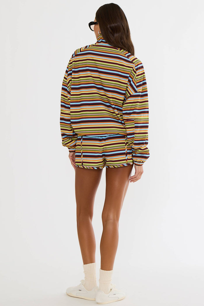 A model shown from the back wearing a colorful horizontally striped long-sleeve shirt and matching shorts set. The stripes feature yellow, blue, red, and brown tones on a light base, paired with white socks and white sneakers against a plain white studio background.