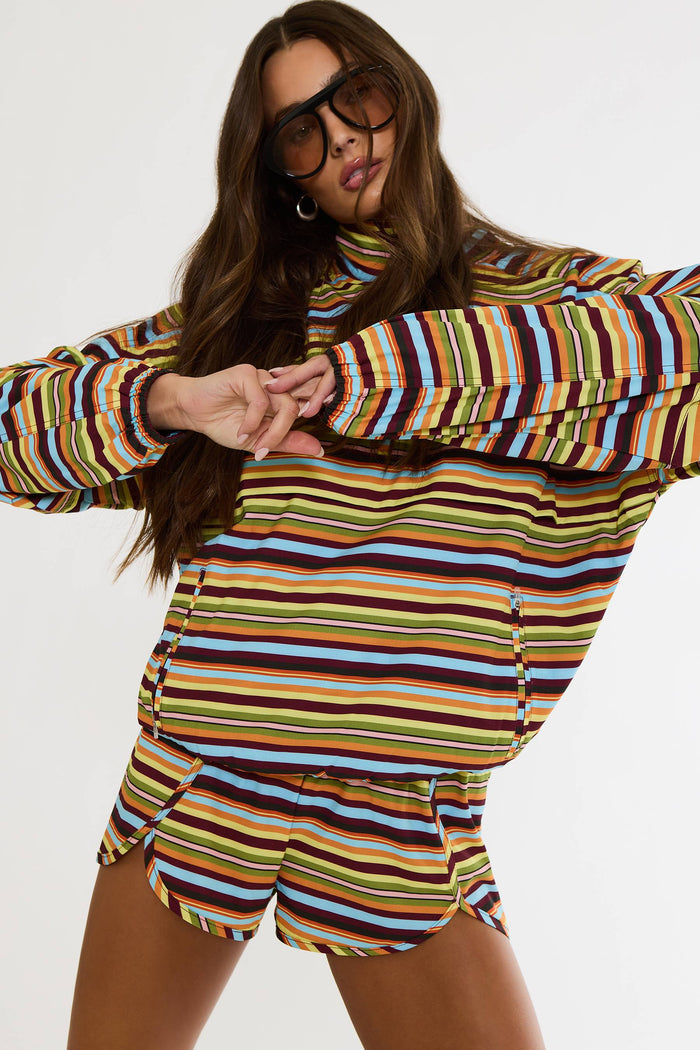 A woman modeling a matching two-piece set featuring a colorful horizontal striped long-sleeve top and shorts in shades of yellow, blue, brown, orange, and white, set against a plain white background.