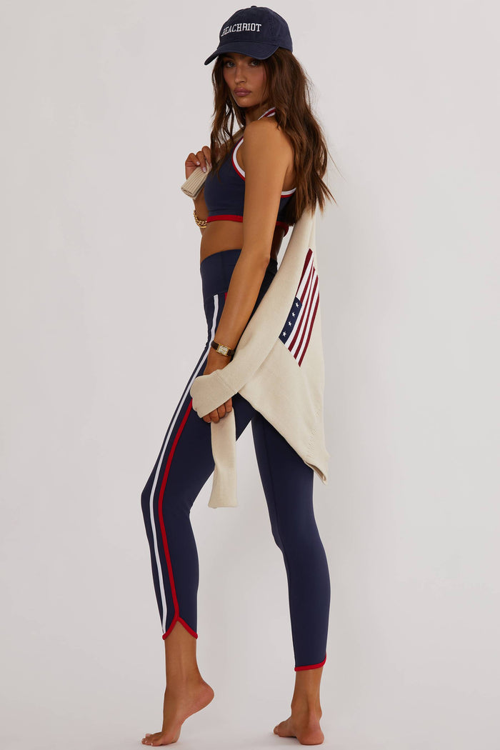 A woman posing in blue and multi-colored active wear leggings with a sports bra and a cap, the outfit features a stars and stripes pattern.