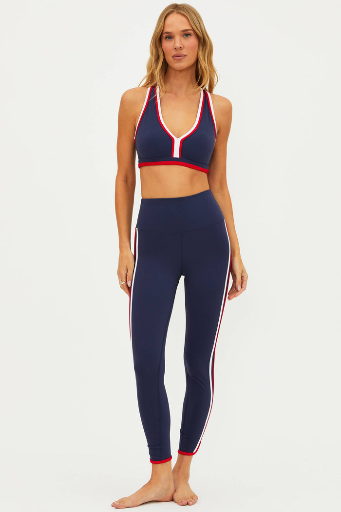 A woman posing in blue and multi-colored active wear leggings with a sports bra and a cap, the outfit features a stars and stripes pattern.