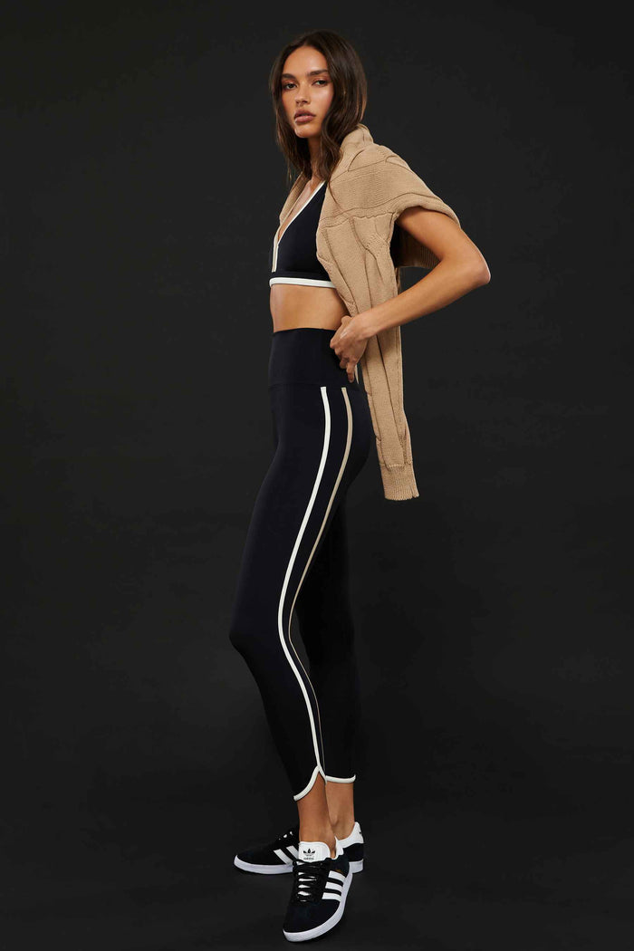 A model wearing high-waisted black leggings with colorblock detailing on the sides and a matching sports bra.