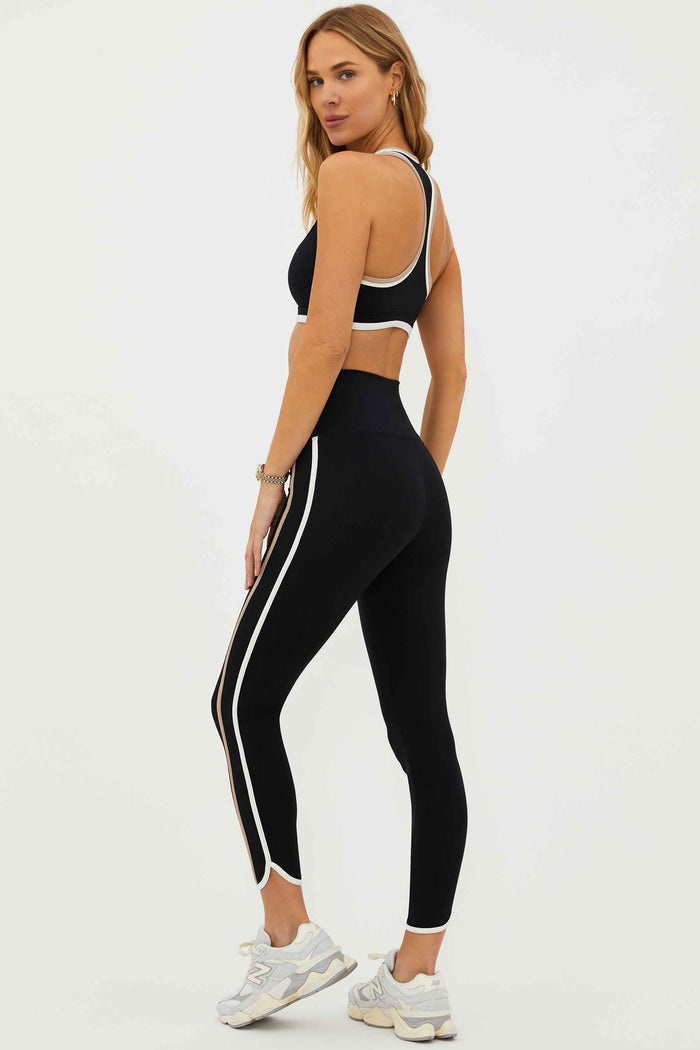 A model wearing high-waisted black leggings with colorblock detailing on the sides and a matching sports bra.
