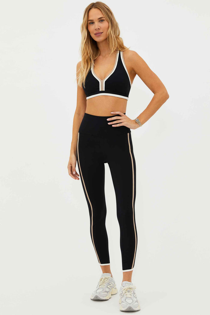 A model wearing high-waisted black leggings with colorblock detailing on the sides and a matching sports bra.