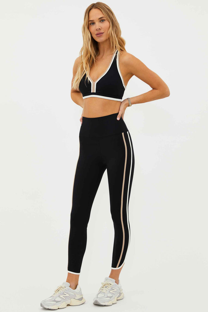 A model wearing high-waisted black leggings with colorblock detailing on the sides and a matching sports bra.