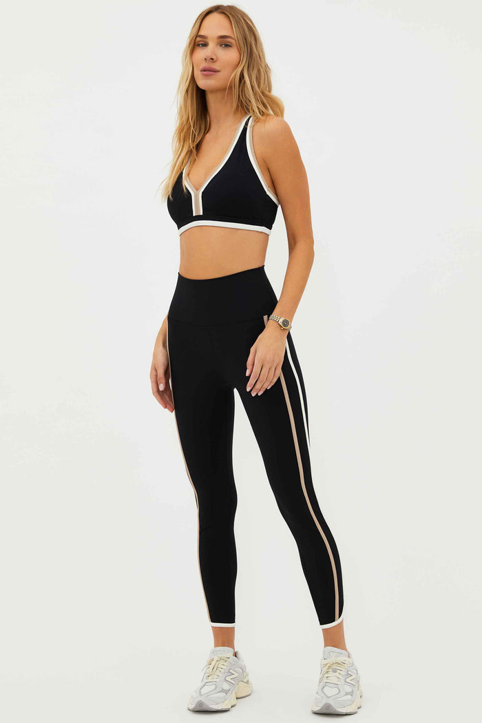 A model wearing high-waisted black leggings with colorblock detailing on the sides and a matching sports bra.