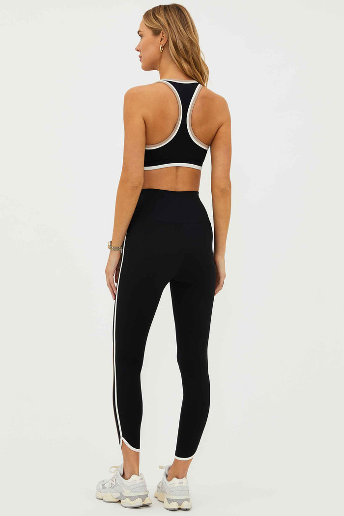 A model wearing high-waisted black leggings with colorblock detailing on the sides and a matching sports bra.