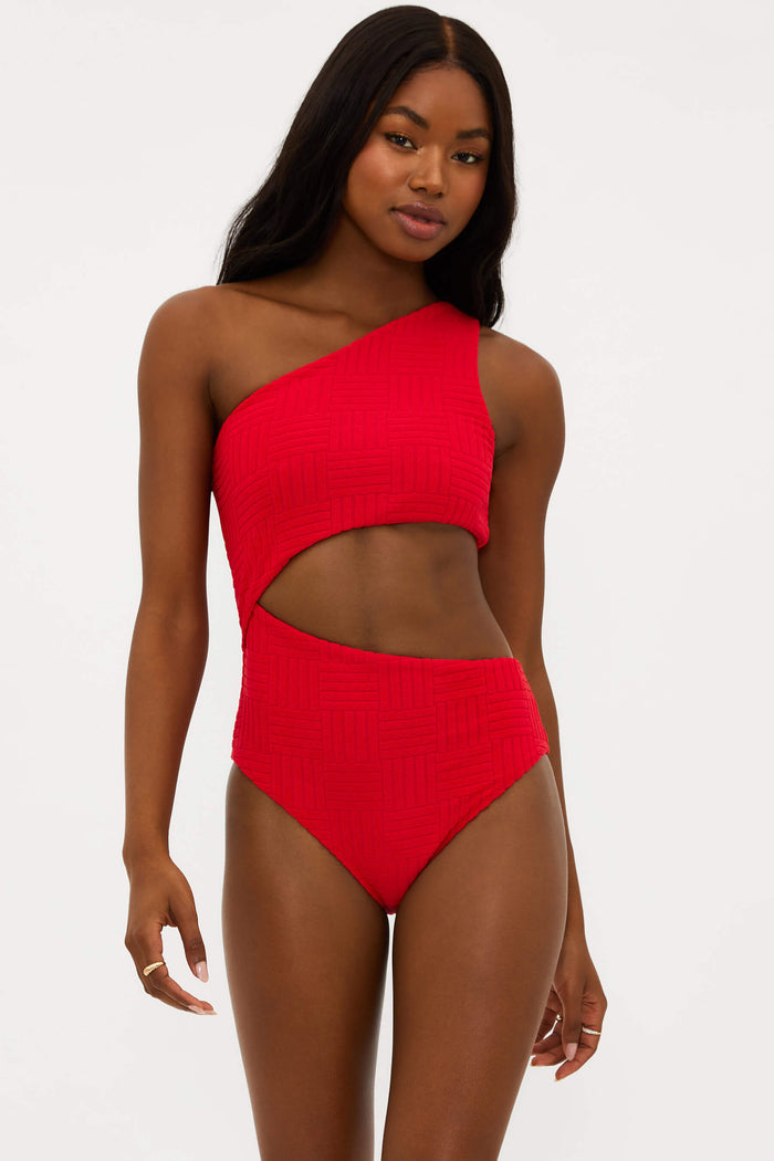 A model wearing a red asymmetrical one-piece swimsuit with side cutouts.