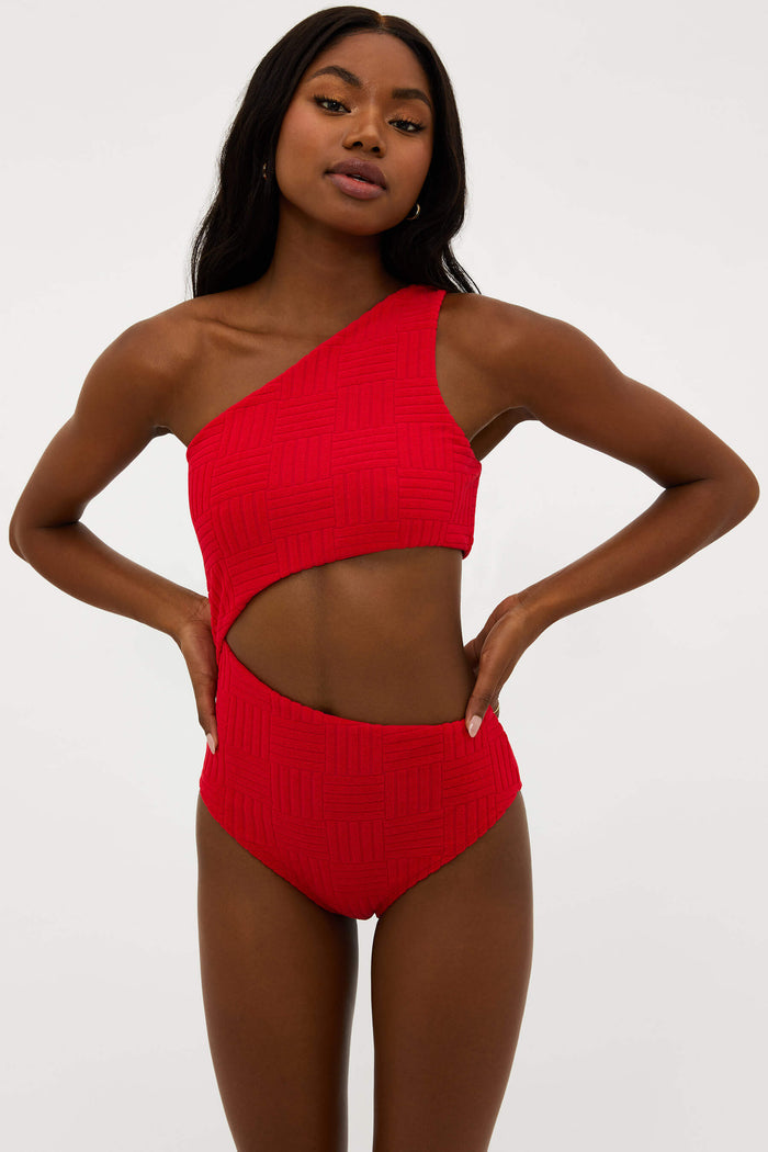 A model wearing a red asymmetrical one-piece swimsuit with side cutouts.