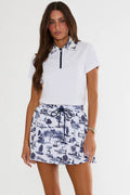 Woman wearing a white polo shirt and blue patterned skirt on a white background