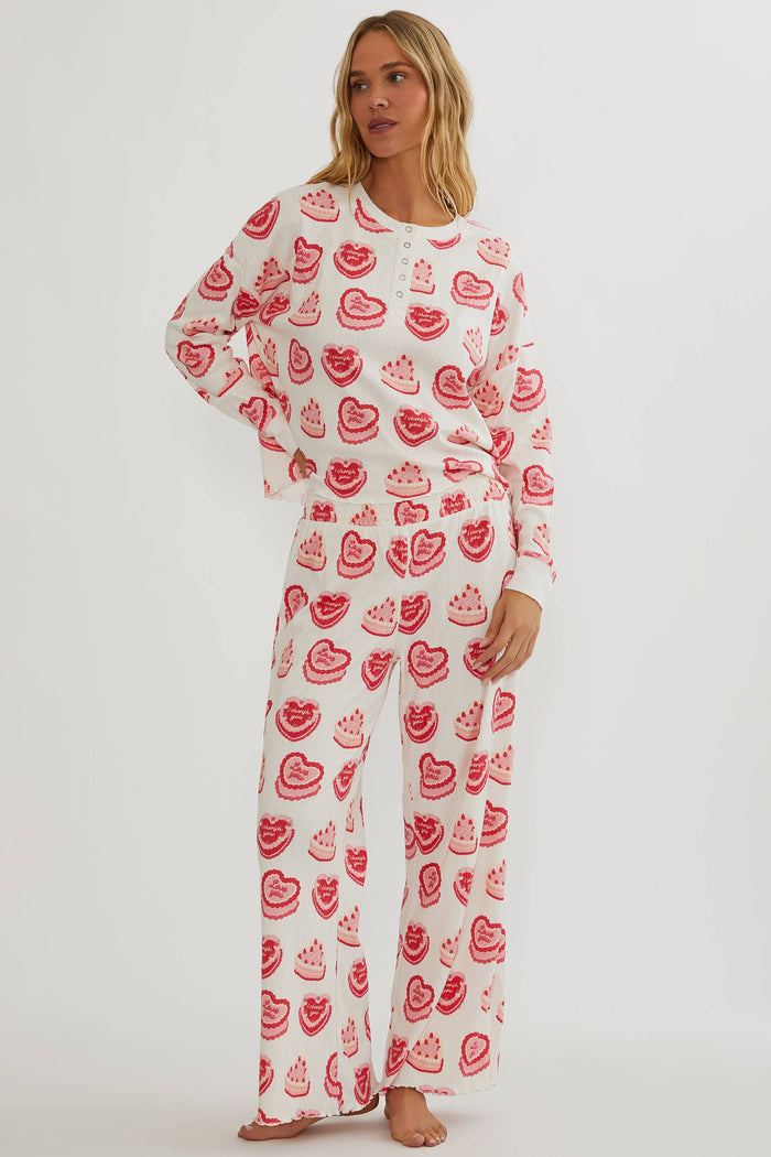 Woman wearing a white outfit with red heart patterns on a plain background