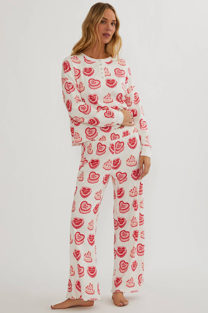 Woman wearing a white pajama set with red heart patterns on a plain background