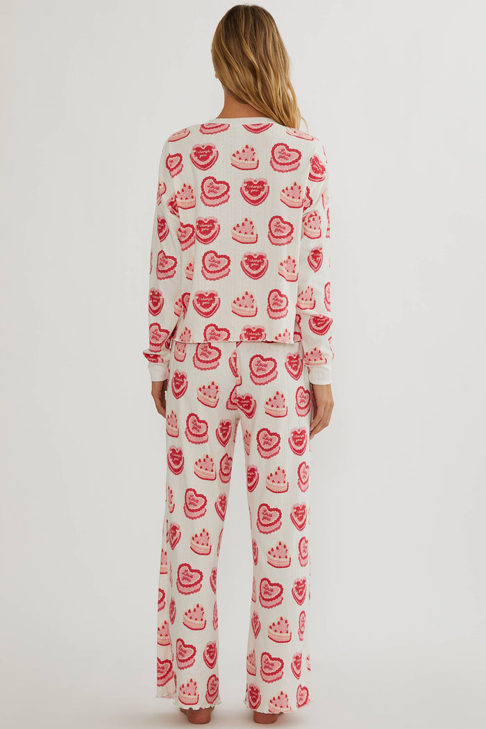 Person wearing a white pajama set with red heart patterns on a plain background