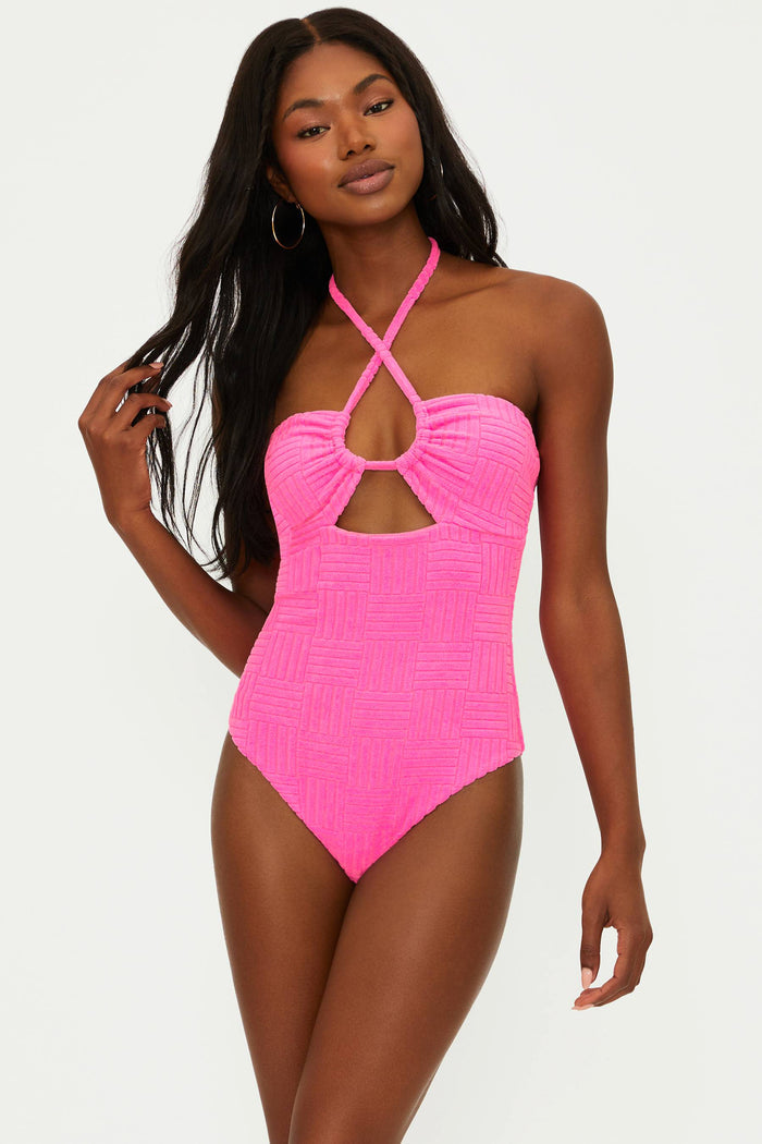 A model wearing a pink one-piece swimsuit with an adjustable halter neck and cut-out detail.