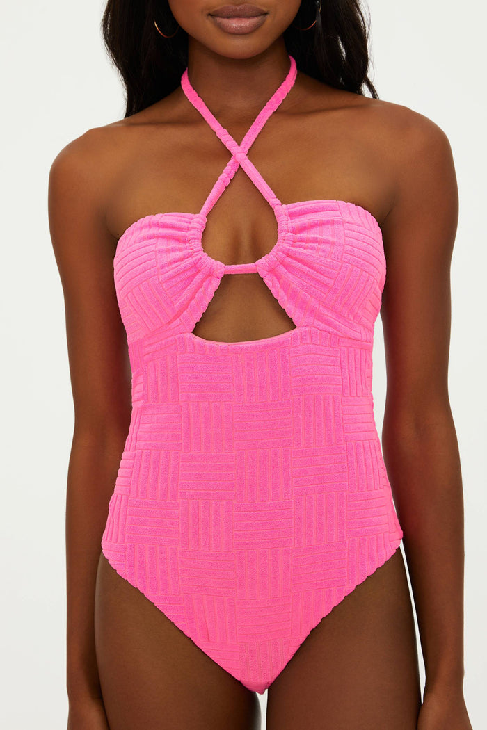 A model wearing a pink one-piece swimsuit with an adjustable halter neck and cut-out detail.