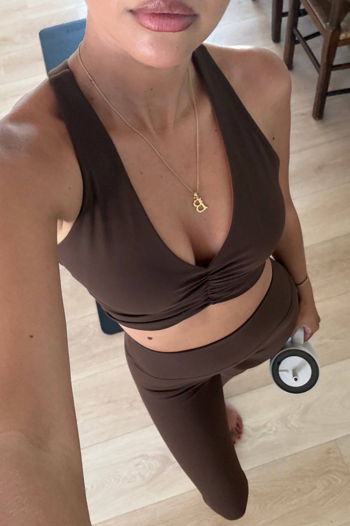 Person wearing a brown sports bra and leggings holding a dumbbell indoors.