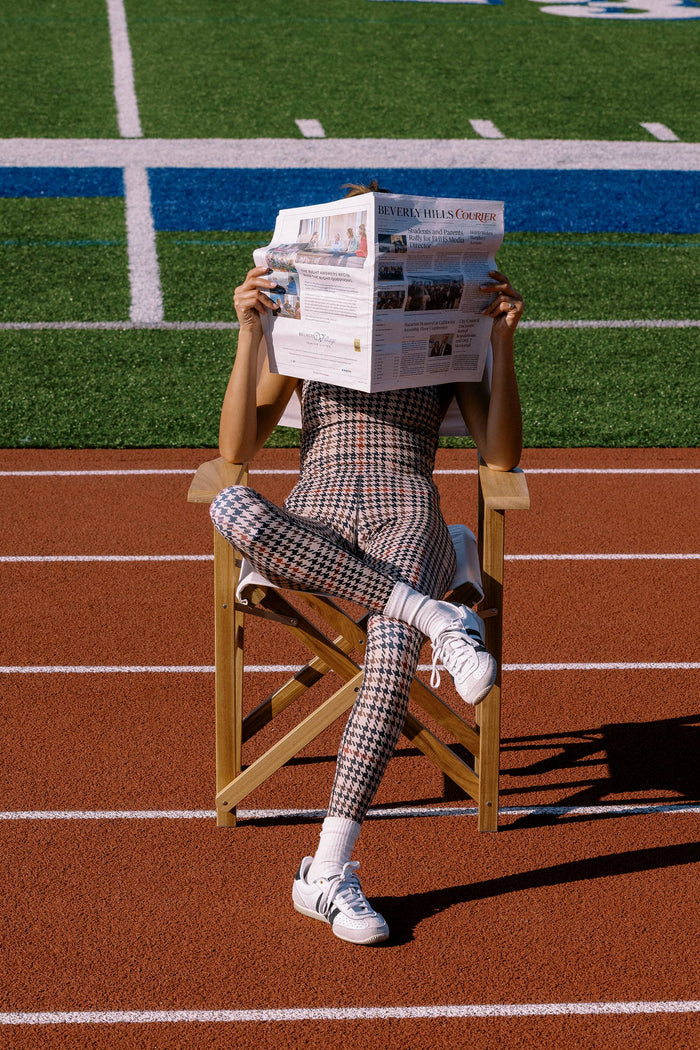 Person sitting on a director's chair on a running track, reading a newspaper.