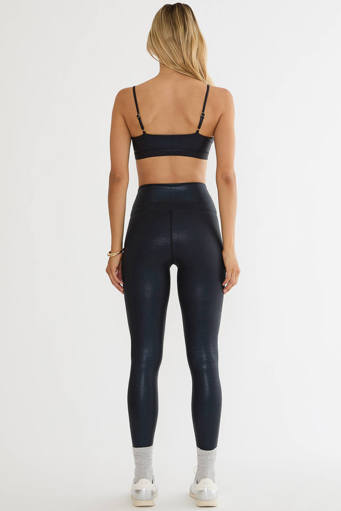 Woman wearing black shiny leggings on a plain white background.