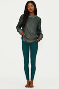 Woman wearing a dark green ribbed sweater and teal leggings on a white background