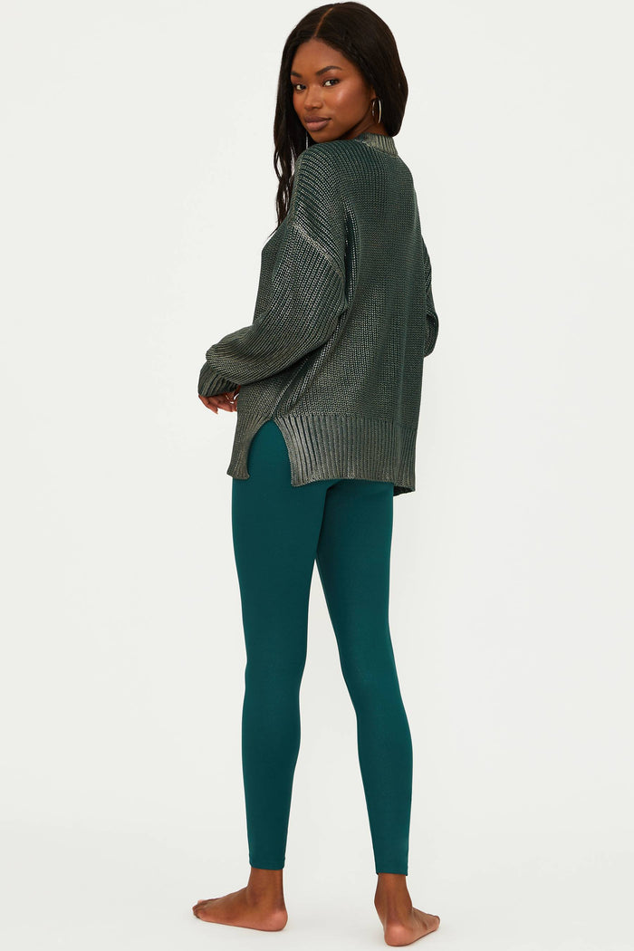 Woman wearing a dark green ribbed sweater and teal leggings on a white background